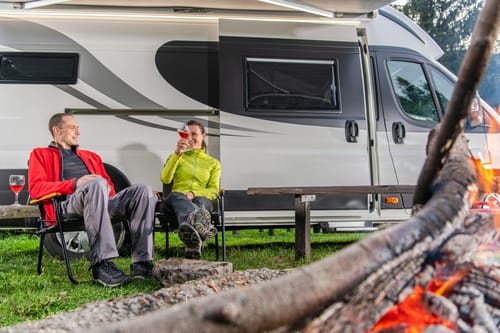 a couple boondocking without hookups in their rv in the woods near a campfire drinking wine